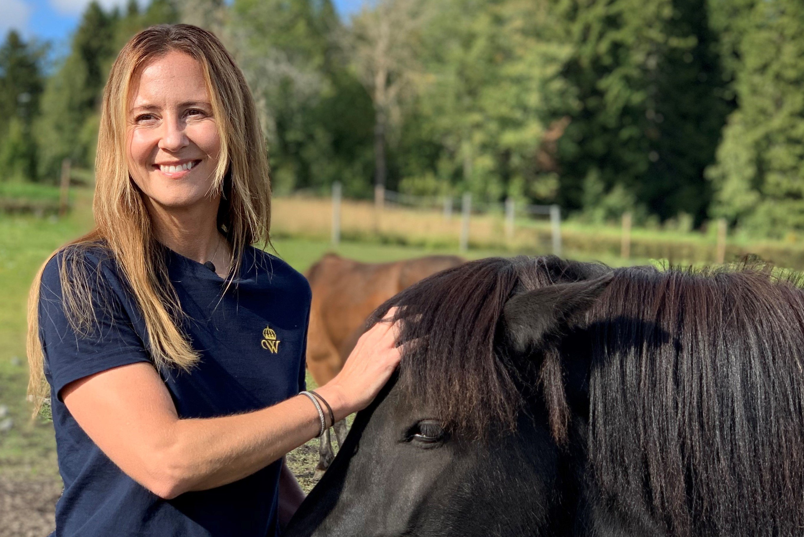 Emma Roos står i hästhage och klappar på islandshäst