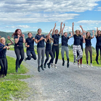 En grupp glada ungdomar hoppar upp och håller händerna i luften. De är glada. Det är en fin sommardag på Wången.