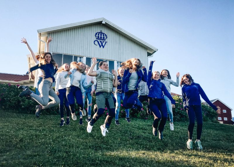 15 glada tjejer på en grön gräsmatta hoppar upp i luften. Alla deltagare på 2018-års islandshästridläger
