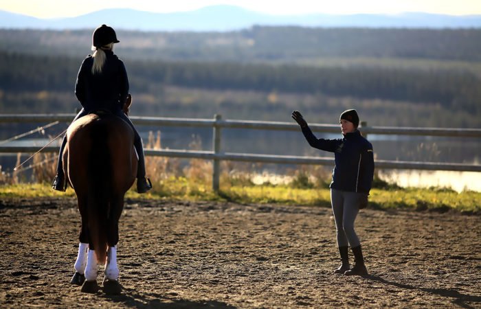 Ridlärare står i en paddock och ger anvisningar till en ryttare till häst