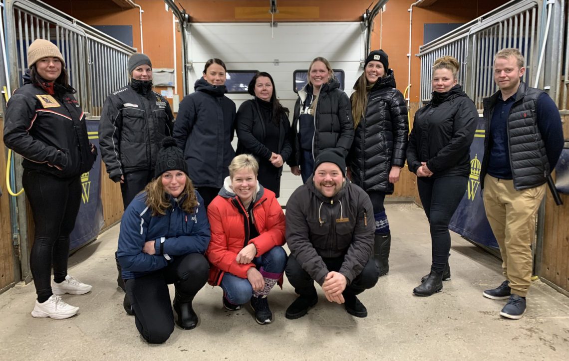 Elva personer i vinterkläder samlade i ett av stallen på Wången. 9 kvinnor och 2 män som är redo att bli proffstränare