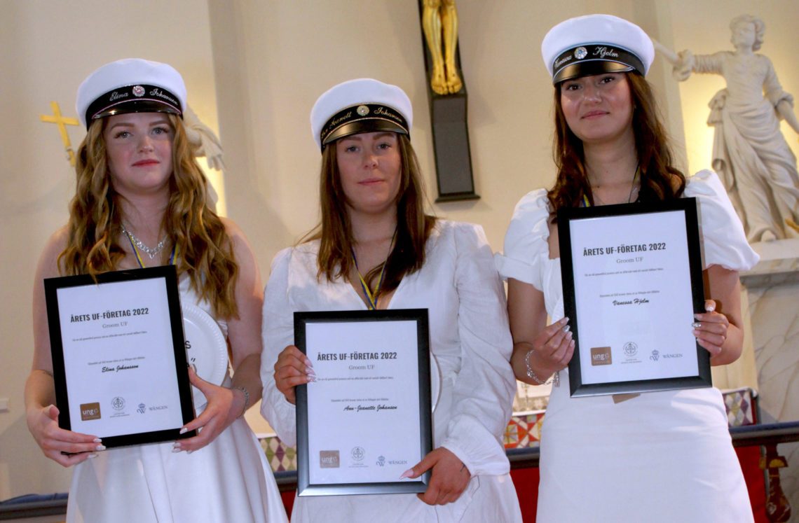 Tre flickor i studentkläder håller i diplom i kyrkan
