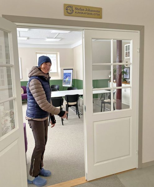 I dörröppningen mellan vita dörrar med spröjsade glas står Pia Tillberg och välkomna in till biblioteket. 