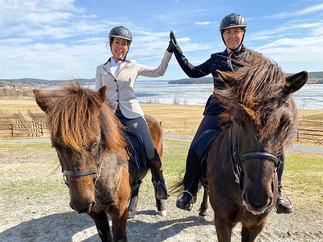 Två kvinnor till häst ger varandra en high five efter de klarat Ridlärare IV-utbildningen