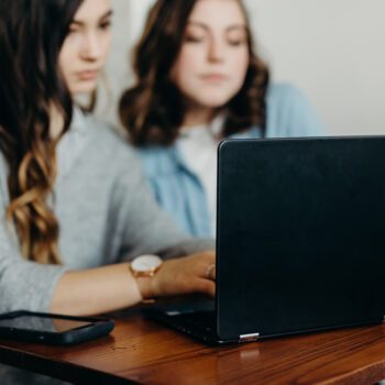 Två kvinnor sitter bakom en dator.