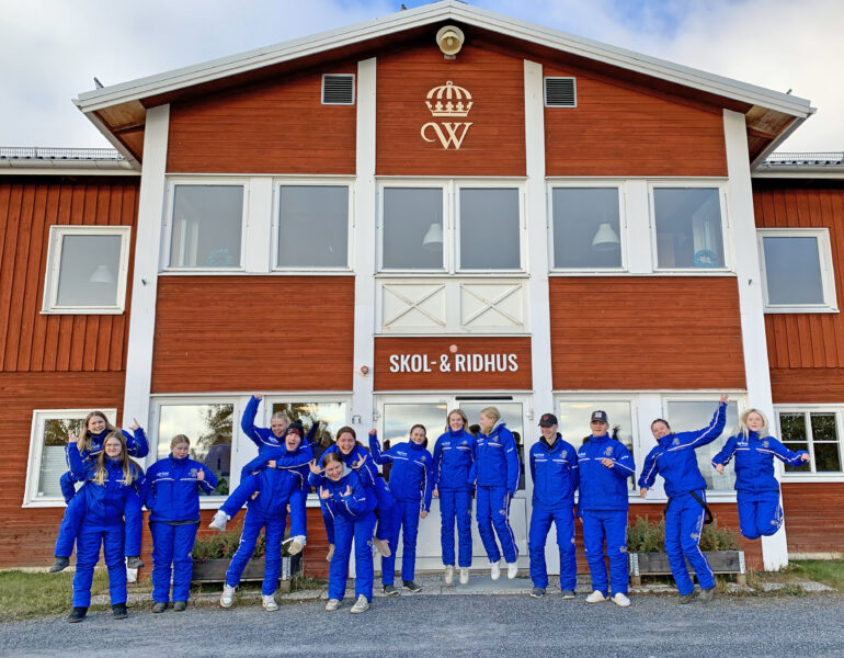 Glada ungdomar iklädda blåa travdressar utanför ingången till Wångens röda skolhus