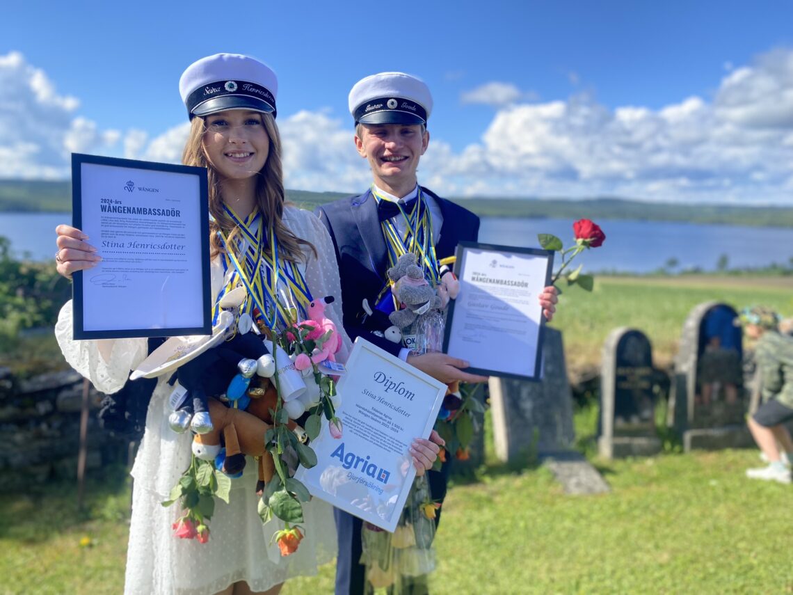 Stina och Gustav står finklädda med studentmössorna på runt halsen har de blågula band med blommor hängandes. I händerna håller de stipendierna. Det är en vacker sommardag. I bakgrunden syns Alsensjön.